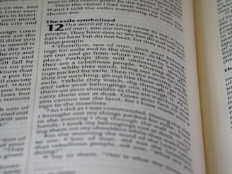 A close-up image of a book page showing text in English, discussing themes related to exile and the word of the Lord. The text includes a passage from the Bible, with some words in bold. The page appears slightly angled, and the focus is primarily on the left side.