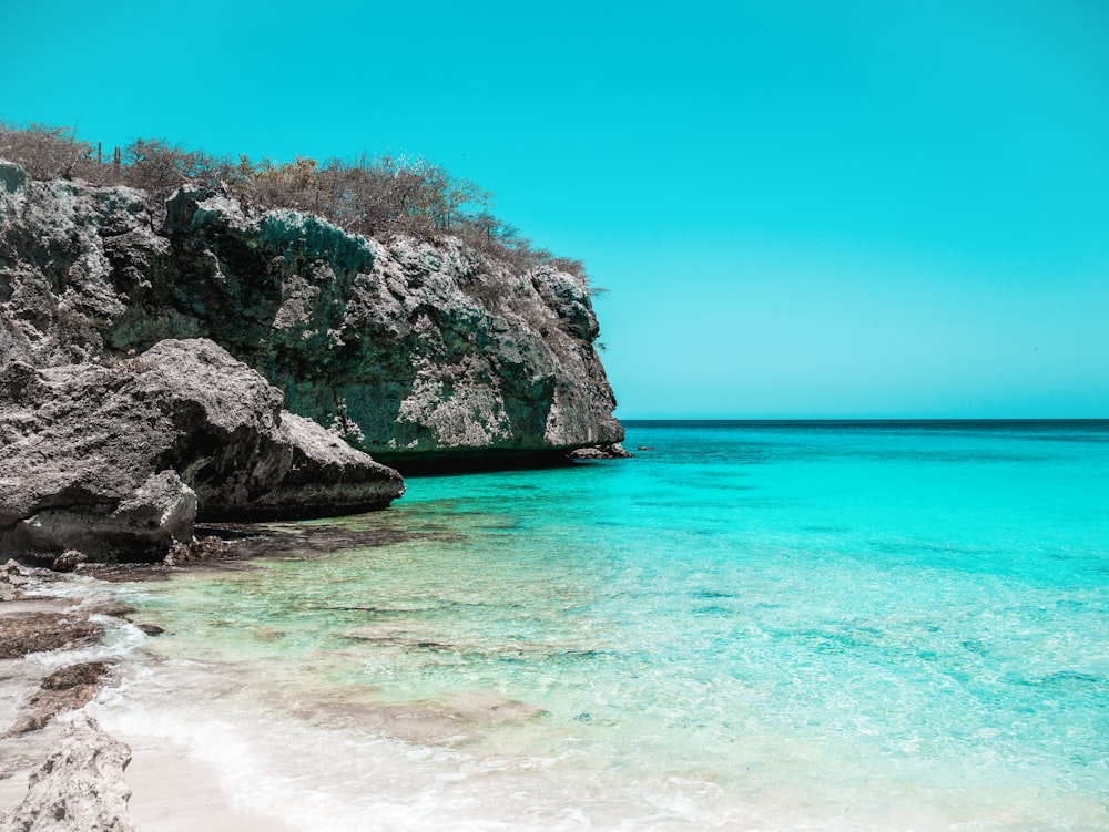 a beach with clear blue water next to a cliff