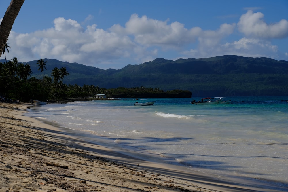 a sandy beach with a boat in the water and mountains in the background