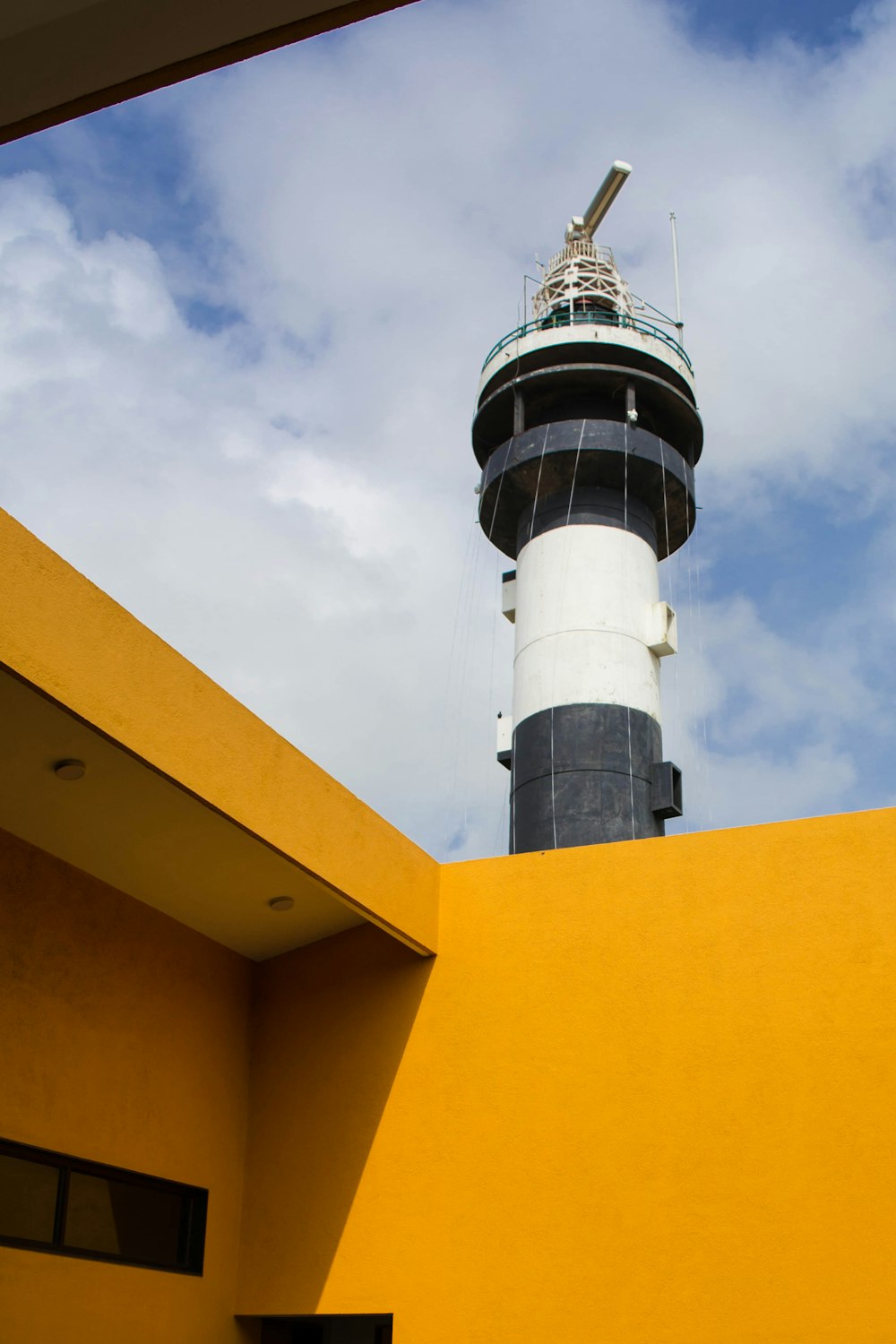 a tall white and black lighthouse on top of a yellow building