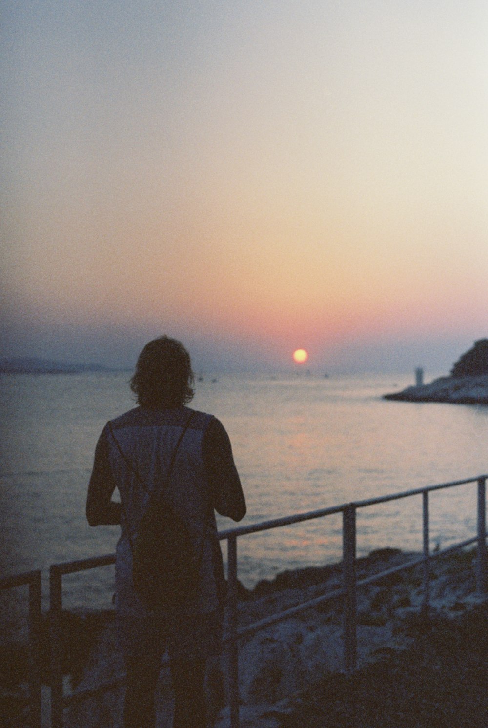 uma pessoa em pé em uma praia observando o pôr do sol