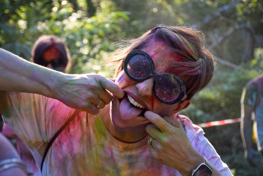 Une femme est couverte de poudre colorée et tient une paire de lunettes contre elle