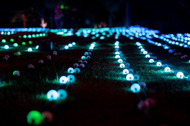 An outdoor night scene showing a cluster of uniquely designed glowcraft bottles lighting a garden party.