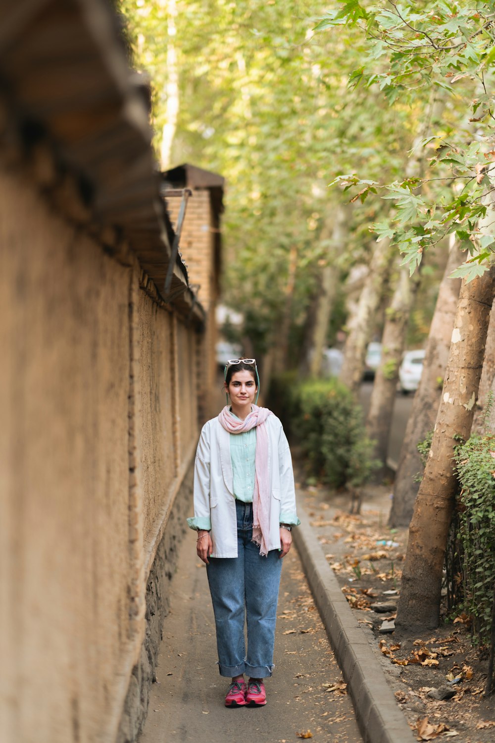 a woman walking down a sidewalk next to a wall