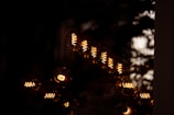 Multiple Edison-style light bulbs with glowing filaments are arranged in a pattern against a dark background. The bulbs emit a warm, amber light that contrasts with the surrounding darkness, creating a striking visual effect.
