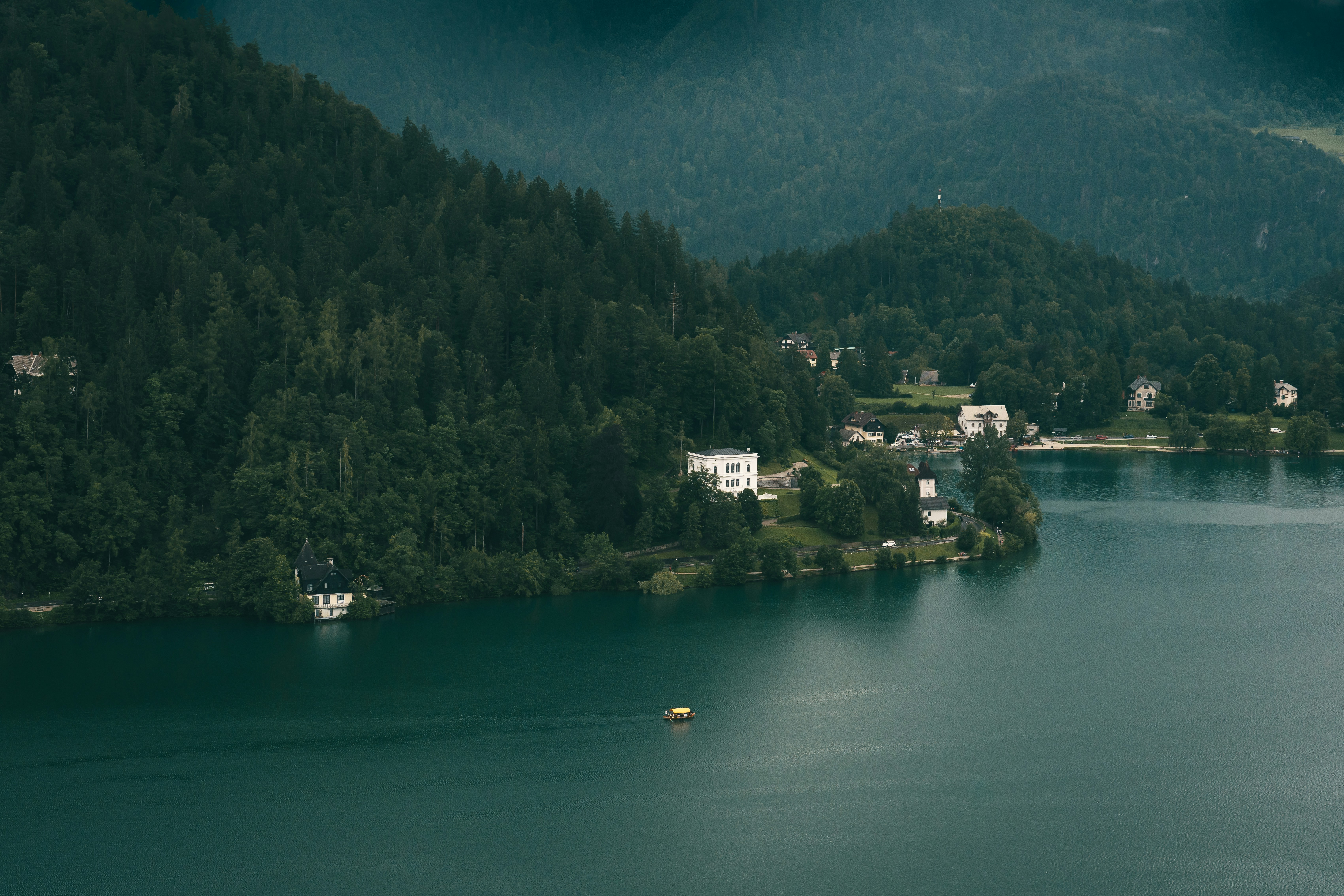 a body of water surrounded by a forest, Yellow boat on Lake Bled, Slovenia