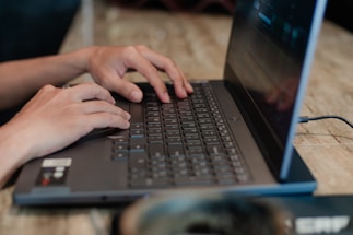 Close-up of hands typing on a laptop keyboard with electronic components nearby.