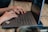 Close-up of hands typing on a laptop keyboard with coffee nearby.