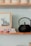 A shelf with a black teapot sits next to a small stack of books and a framed abstract painting. The books include titles on artificial intelligence, topped with a loose paper. There are stacked off-white ceramic bowls above.
