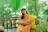 A smiling woman relaxing on a stylish outdoor loveseat surrounded by greenery.