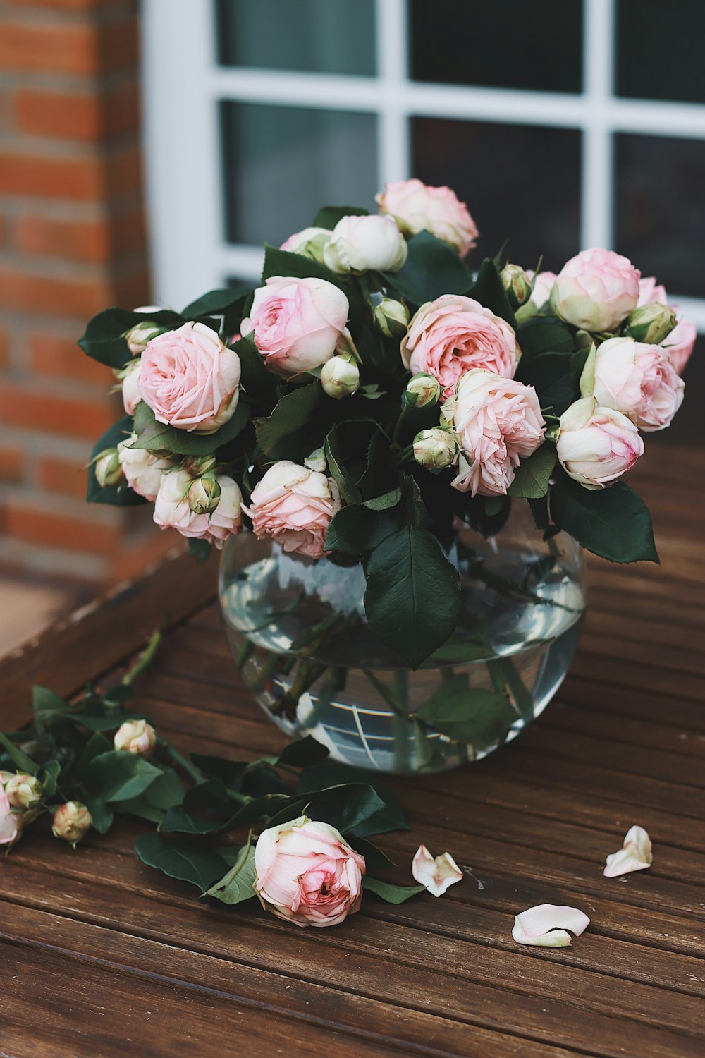 a glass vase filled with pink roses on top of a wooden table