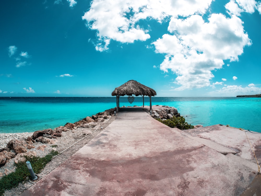 a pier with a thatched roof over the ocean