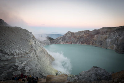 A scenic view of Kawah Putih with tourists admiring the turquoise crater lake surrounded by mist.