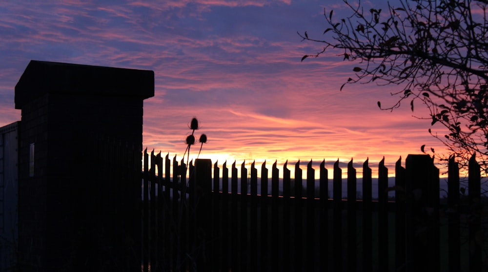 the sun is setting behind a fence and a building