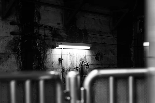 A dimly lit industrial pipe dripping rainwater against a backdrop of flickering fluorescent lights and tangled wires.