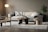 A modern living room with a beige sofa adorned with plush pillows and a patterned cushion. The room features a round wooden coffee table with decorative items. A stylish chair with a woven seat and a distinctive curved chair are positioned on a light gray rug. A soft-lit floor lamp stands on the left, and a lush green plant in a textured black pot is on the right, against a neutral wall.