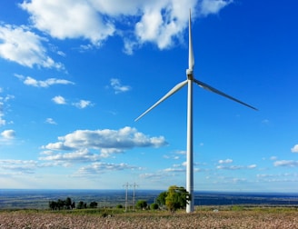 A wind turbine spinning in a green field with a bright horizon.
