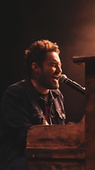 a man singing into a microphone while sitting at a piano