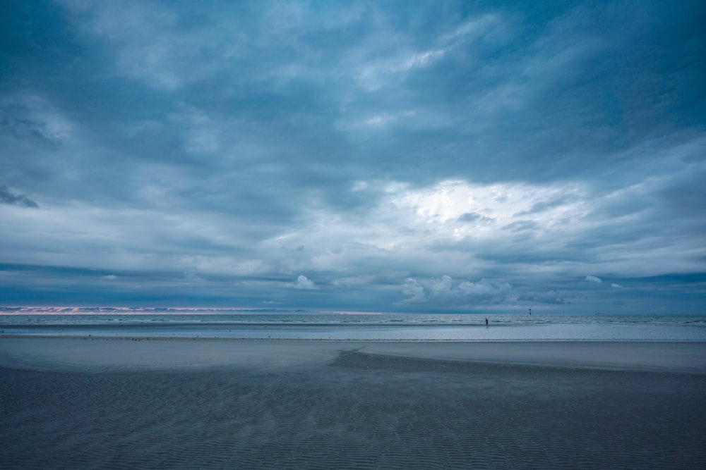 a person walking on a beach under a cloudy sky