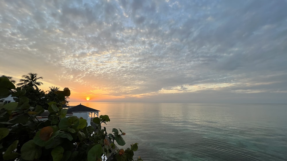 the sun is setting over the ocean with a gazebo in the foreground