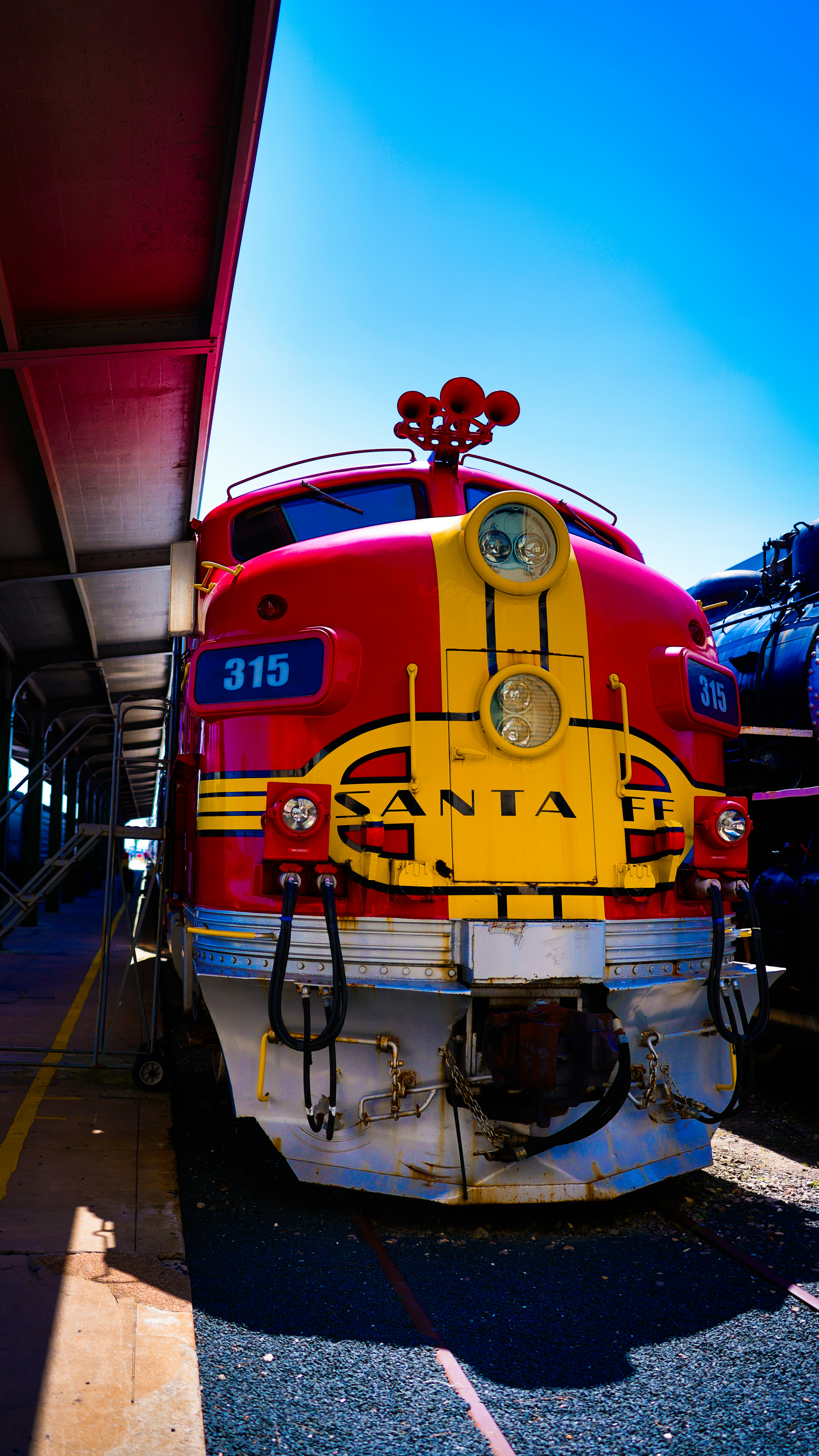 A red and yellow train parked next to a train station photo – Free