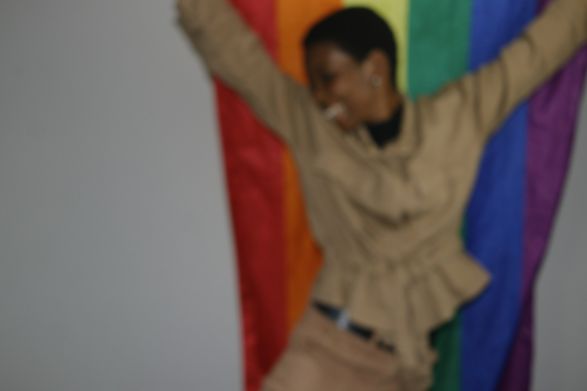 A candid photo of George smiling broadly under a bright rainbow banner, embodying the spirit of his sunny personality.