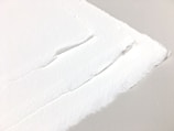 A close-up view of torn edges of thick, textured paper stacked in layers. The paper exhibits a rough, fibrous quality, with the edges appearing frayed and irregular.
