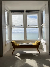 A bright, tidy living room in a sea-front holiday apartment with sunlight streaming through large windows.