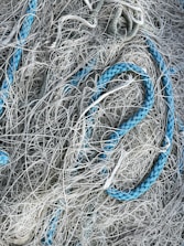 A chaotic tangle of ropes and nets, with strands interwoven in a complex pattern. Some ropes are thick and blue, contrasting with thinner, grayish-white netting.