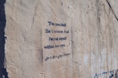 A textured concrete wall features a piece of graffiti with stencil-style text in both English and another language. The poem expresses introspection and connection, with a focus on finding oneself in another's eyes.