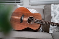 An acoustic guitar resting on a soft cushion next to a handwritten songbook in Spanish.