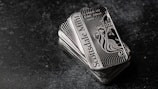 A stack of shiny rectangular silver bars with intricate designs and the inscription 'Scottsdale Mint'. The bars feature a depiction of a lion and have text indicating purity and weight, 'FINE Silver .999'. The background is a dark textured surface, providing contrast to the reflective nature of the bars.