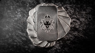 A stack of intricately designed rectangular silver bars with a lion's head wearing a crown engraved in the center. The bars have a textured pattern resembling a spiral, creating an elegant and regal appearance. The background is a dark, marbled surface that enhances the metallic shine of the bars.