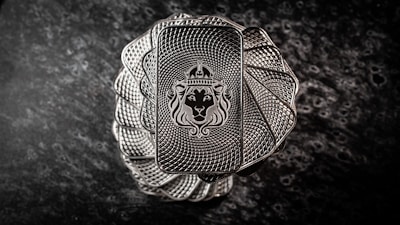 A stack of intricately designed rectangular silver bars with a lion's head wearing a crown engraved in the center. The bars have a textured pattern resembling a spiral, creating an elegant and regal appearance. The background is a dark, marbled surface that enhances the metallic shine of the bars.