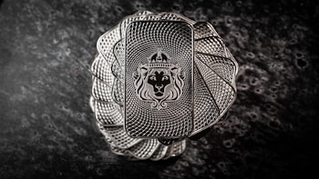 A stack of intricately designed rectangular silver bars with a lion's head wearing a crown engraved in the center. The bars have a textured pattern resembling a spiral, creating an elegant and regal appearance. The background is a dark, marbled surface that enhances the metallic shine of the bars.