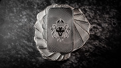 A stack of intricately designed rectangular silver bars with a lion's head wearing a crown engraved in the center. The bars have a textured pattern resembling a spiral, creating an elegant and regal appearance. The background is a dark, marbled surface that enhances the metallic shine of the bars.