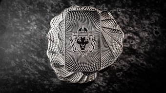 A stack of intricately designed rectangular silver bars with a lion's head wearing a crown engraved in the center. The bars have a textured pattern resembling a spiral, creating an elegant and regal appearance. The background is a dark, marbled surface that enhances the metallic shine of the bars.