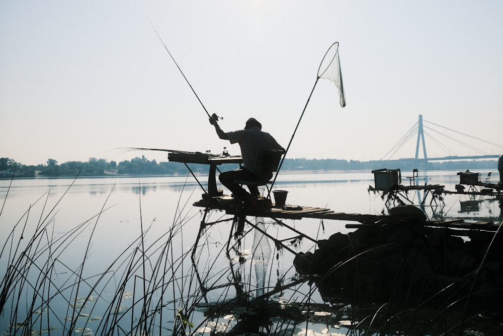 a man sitting on a dock holding a fishing pole