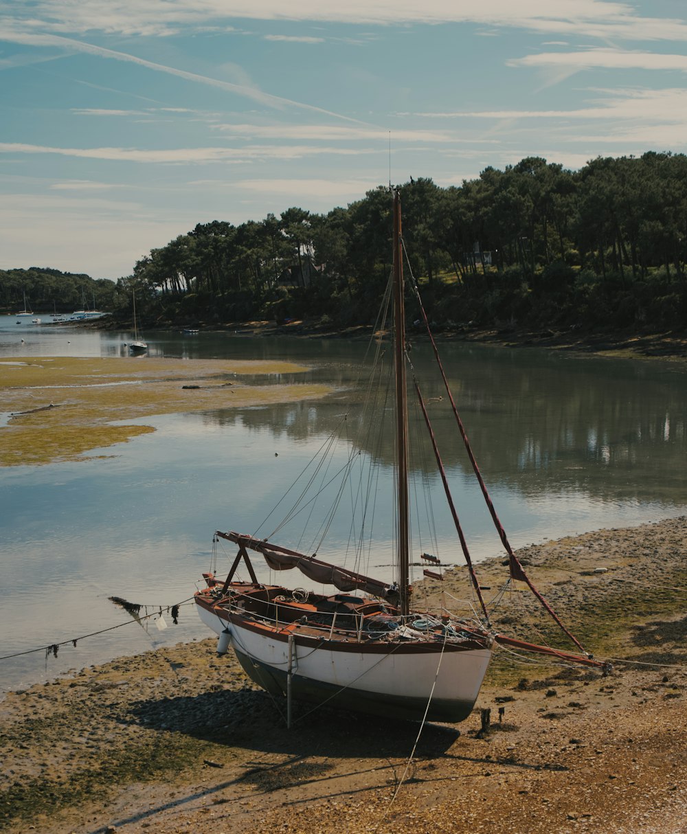 a small sailboat sitting on the shore of a lake