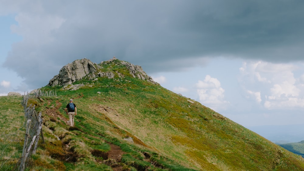 a person walking up a grassy hill on a cloudy day