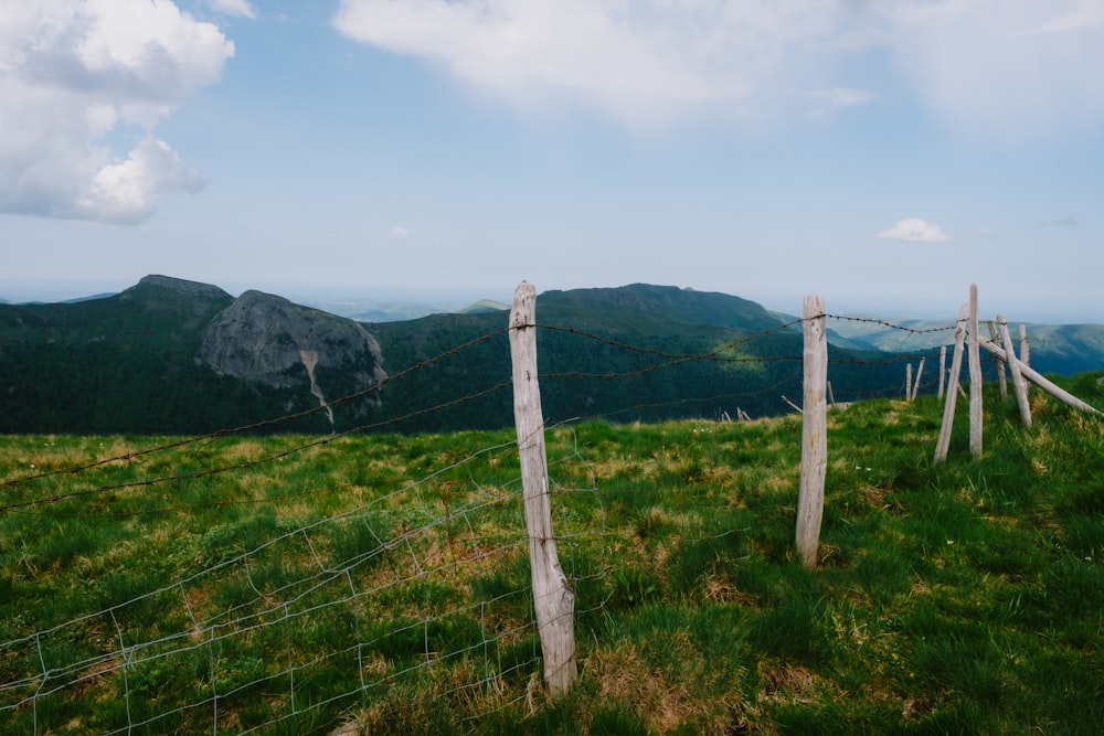 a fence on a grassy hill with mountains in the background