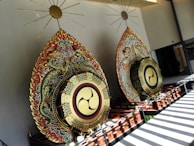 Two large, ornate ceremonial drums are adorned with intricate designs, featuring dragons and vibrant patterns. The drums have a gilded emblem at the center and are set against a modern architectural backdrop with sunlight streaming through, casting shadows on the floor.