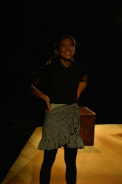 A woman standing confidently with a gentle smile, surrounded by soft light and cultural motifs.