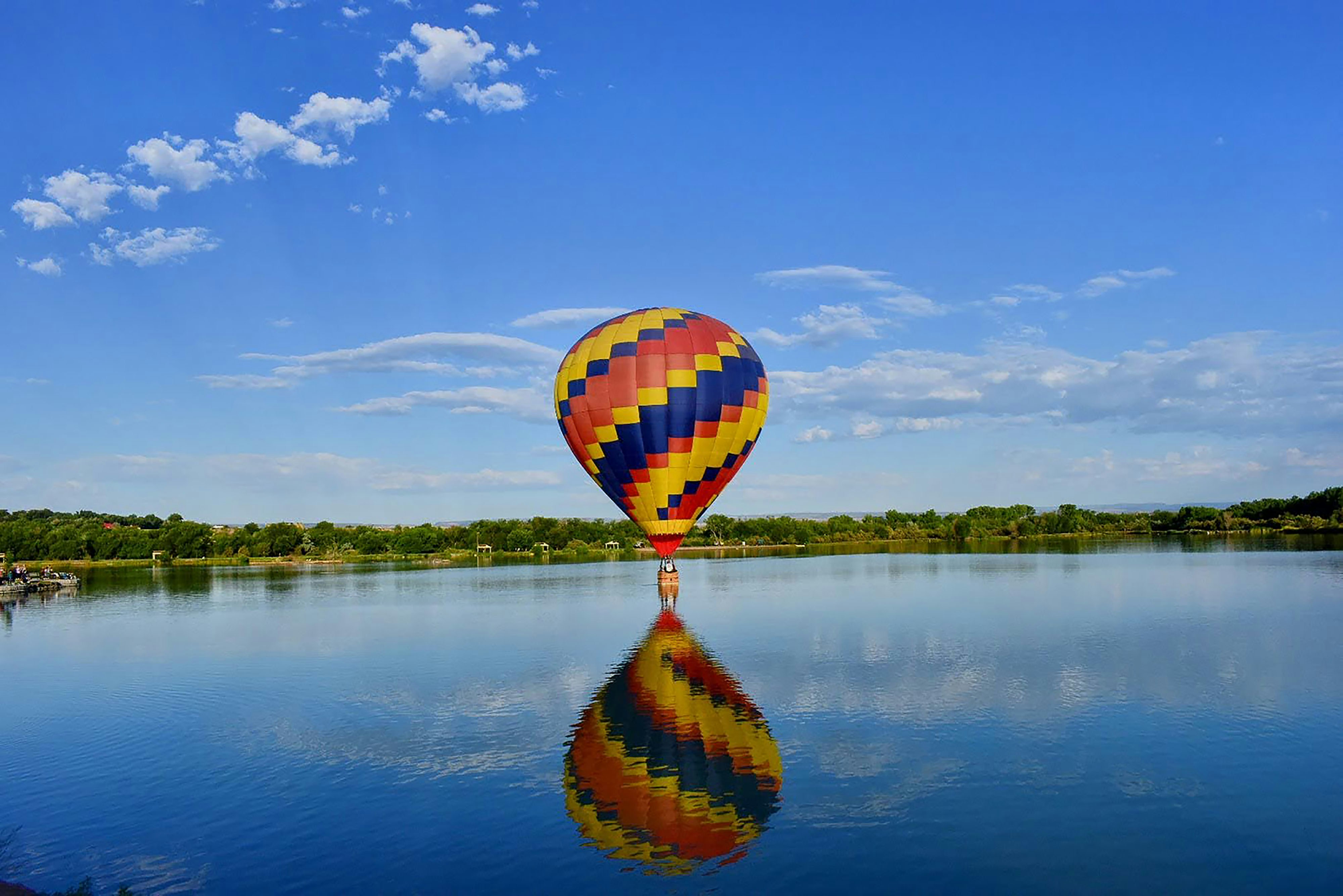 a large colorful hot air balloon flying over a lake