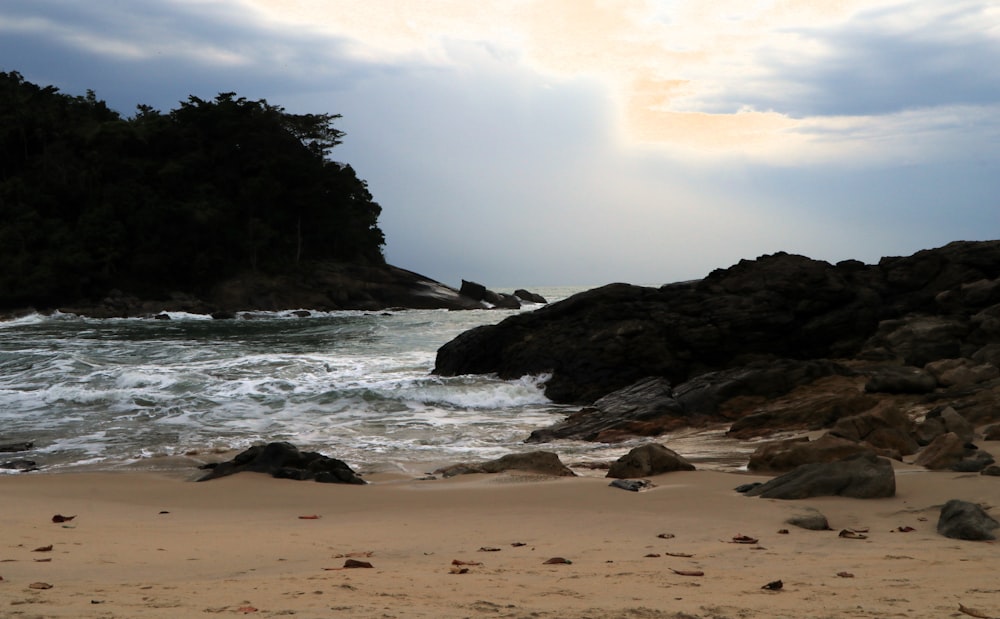 a sandy beach with rocks and water under a cloudy sky