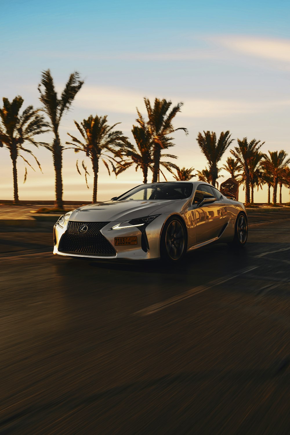 a silver sports car driving down a street next to palm trees