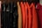 A row of coats hanging on hangers, featuring a variety of colors such as pink, black, beige, orange, and red. The coats are organized neatly in a line, and the material appears to range from fabric to leather.