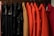 A row of coats hanging on hangers, featuring a variety of colors such as pink, black, beige, orange, and red. The coats are organized neatly in a line, and the material appears to range from fabric to leather.