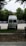 A white van is parked in an open area surrounded by trees. The vehicle is facing away, with a ladder on its rear door, and the brand 'Westfalia' is visible. To the left, several portable toilets are lined up in blue and there are cars parked in the background.