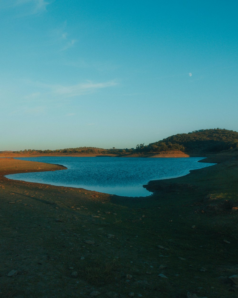 a large body of water sitting next to a lush green field